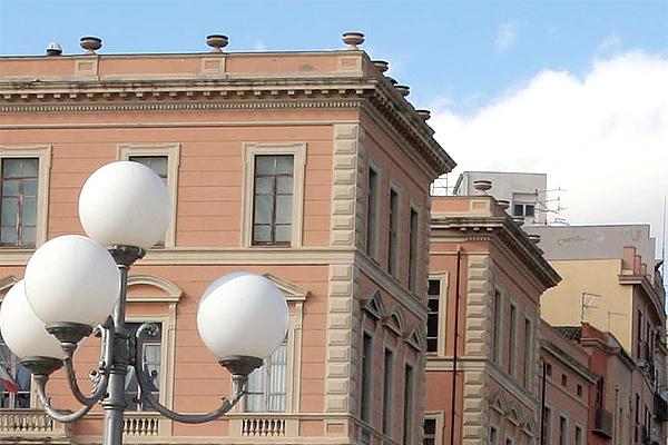 Hellrosa Gebäude mit dekorativem Gesims und Fenstern, daneben eine Straßenlaterne mit vier weißen Kugeln.