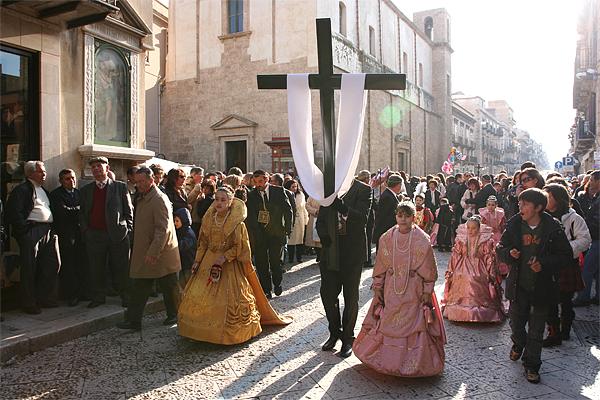 Eine religiöse Prozession auf einer sonnenbeschienenen Straße zeigt Menschen in historischen Kostümen
