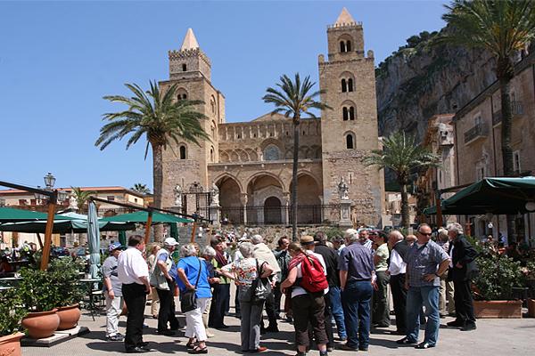 An einem sonnigen Tag steht eine Gruppe Touristen auf einem Platz vor einer großen Kathedrale 
