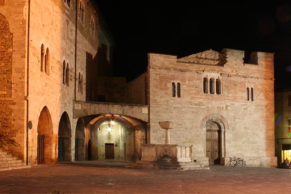 Nachts beleuchtete Steingebäude auf einem italienischen Stadtplatz. Bögen und Fenster sind sichtbar.