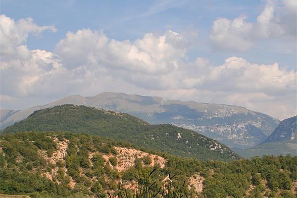Sanfte grüne Hügel und Berge unter einem bewölkten blauen Himmel.