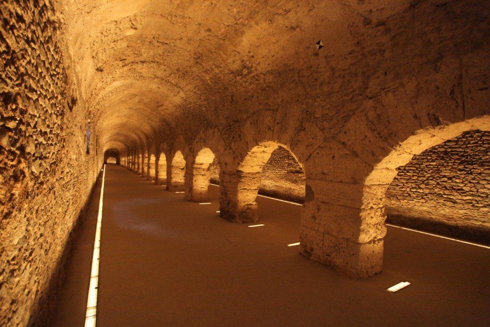 Langer, gewölbter Tunnel mit einer Reihe von Säulen, beleuchtet von warmem Licht