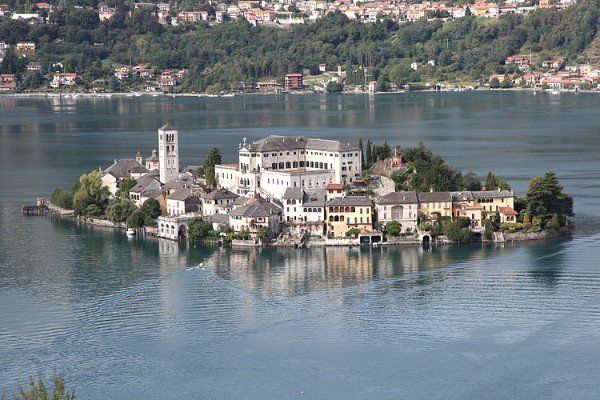 Insel mit Gebäuden, darunter ein hoher Turm, umgeben von ruhigem blauem Wasser. 