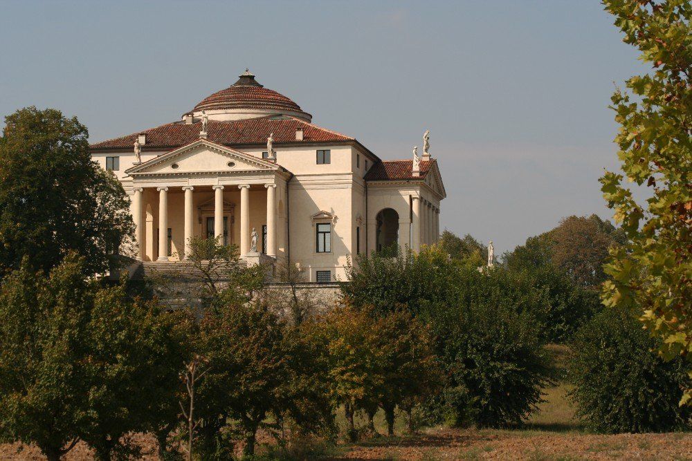 Eine klassische italienische Villa mit Kuppel, auf einem kleinen Hügel gelegen und durch Bäume hindurch zu sehen.