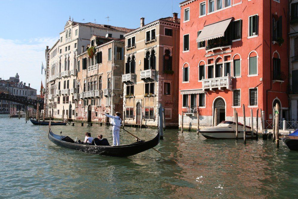 Gondel mit Passagieren in Venedig, vorbei an farbenfrohen Gebäuden entlang eines Kanals; Gondoliere in Weiß.
