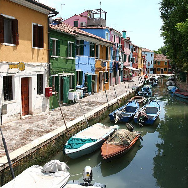 Bunte Häuser säumen einen Kanal im italienischen Burano. Mehrere Boote liegen entlang der Wasserstraße vor Anker.