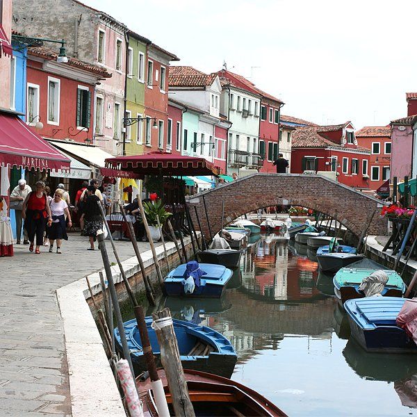 Bunte Gebäude säumen einen Kanal im italienischen Burano. Mehrere Boote liegen am Wasserweg. 