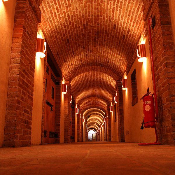 Gemauerter, gewölbter Korridor, beleuchtet von warmem Licht; rechts steht ein Feuerlöscher.