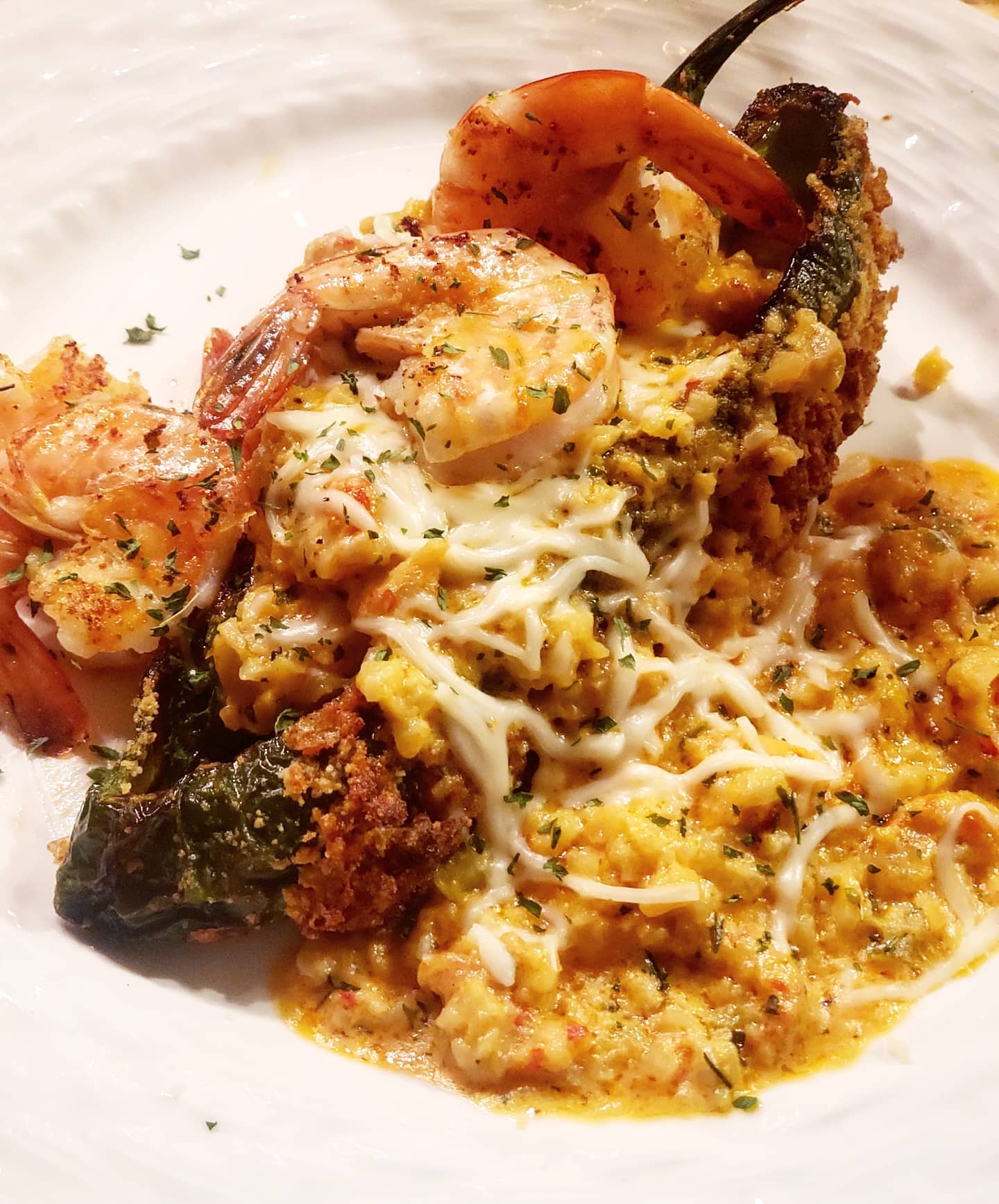 Stuffed poblano pepper with shrimp, melted cheese, and sauce on a white plate.