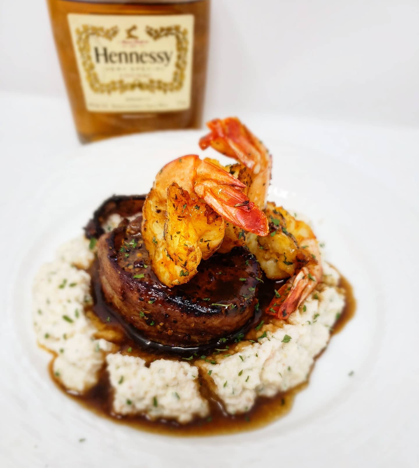 Steak and shrimp dish on grits, with Hennessy bottle in the background.