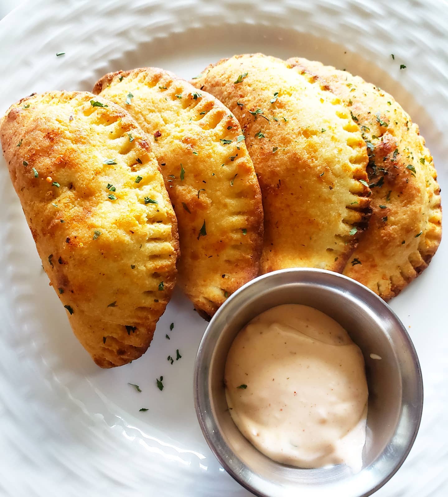 Three golden-brown empanadas on a white plate with a small bowl of dipping sauce.