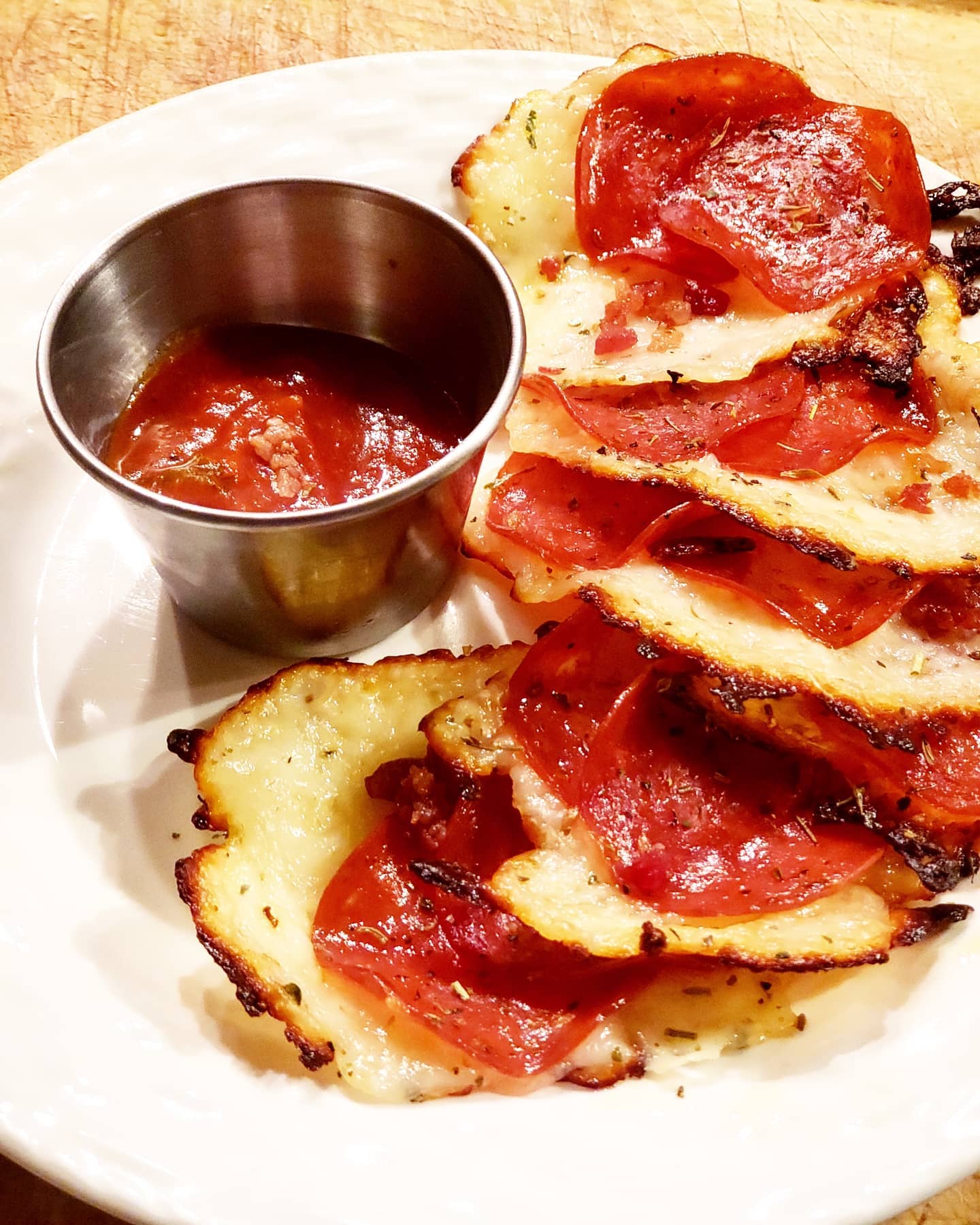 Potato rounds topped with pepperoni, served with red dipping sauce in a metal cup on a white plate.