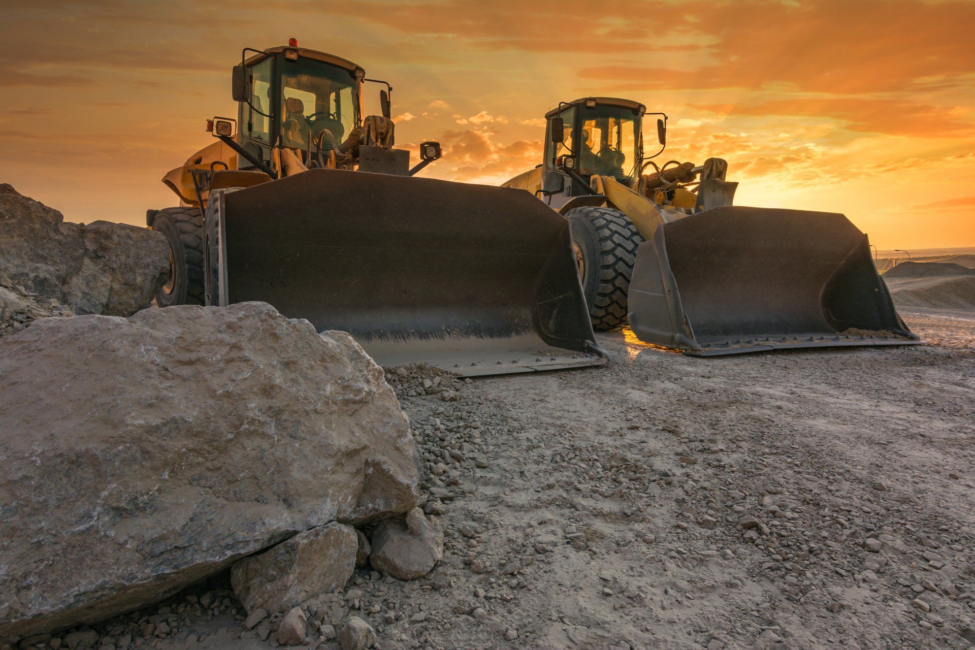 Two bulldozers are working on a construction site at sunset.