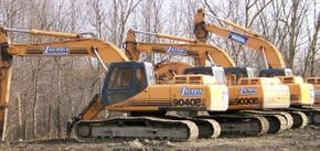 Three yellow excavators are parked next to each other in a dirt field.
