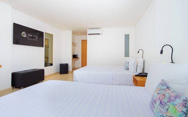 Una habitación de hotel con dos camas queen, sábanas blancas, un televisor y un banco negro.