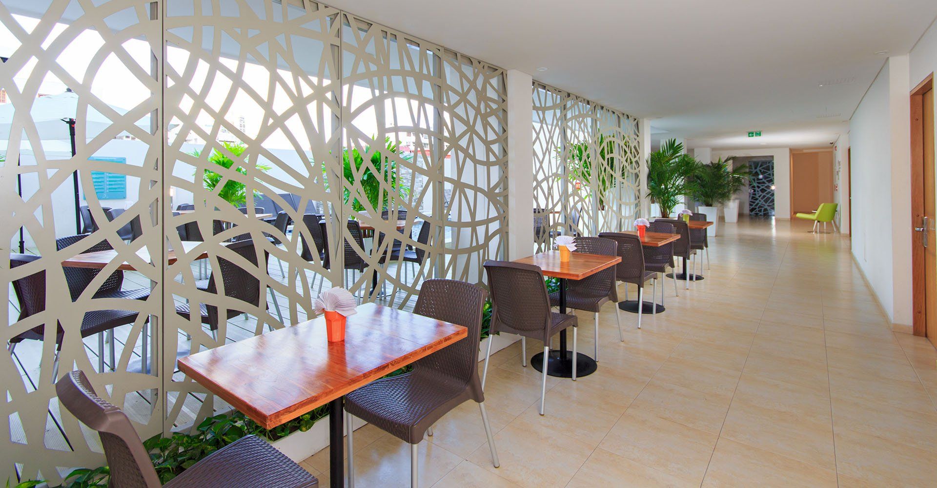 Pasillo de restaurante con mesas y sillas alineadas a lo largo de una pared decorativa.