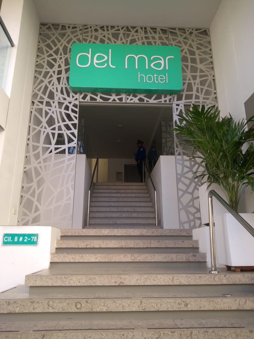 Entrada al Hotel Del Mar. Letrero verde sobre la puerta que da acceso a las escaleras. Paneles blancos decorativos en la pared.