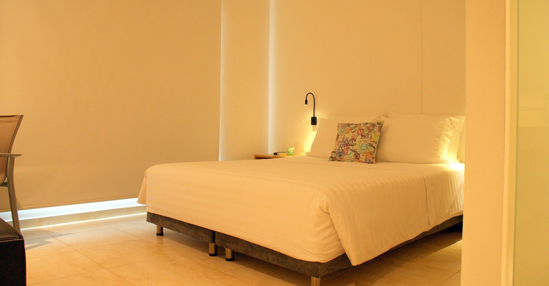 Un dormitorio de hotel luminoso con una cama hecha, una almohada colorida y una silla de escritorio.