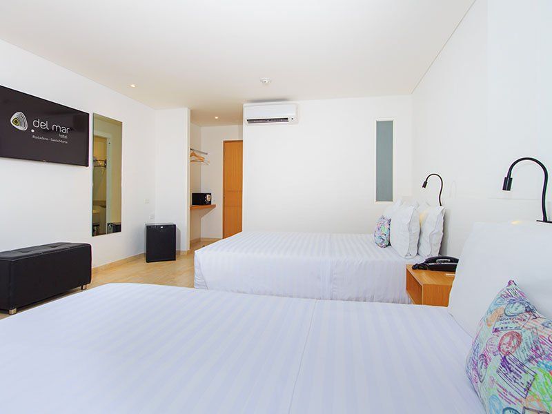 Una luminosa habitación de hotel con dos camas individuales, paredes blancas y un pequeño refrigerador.