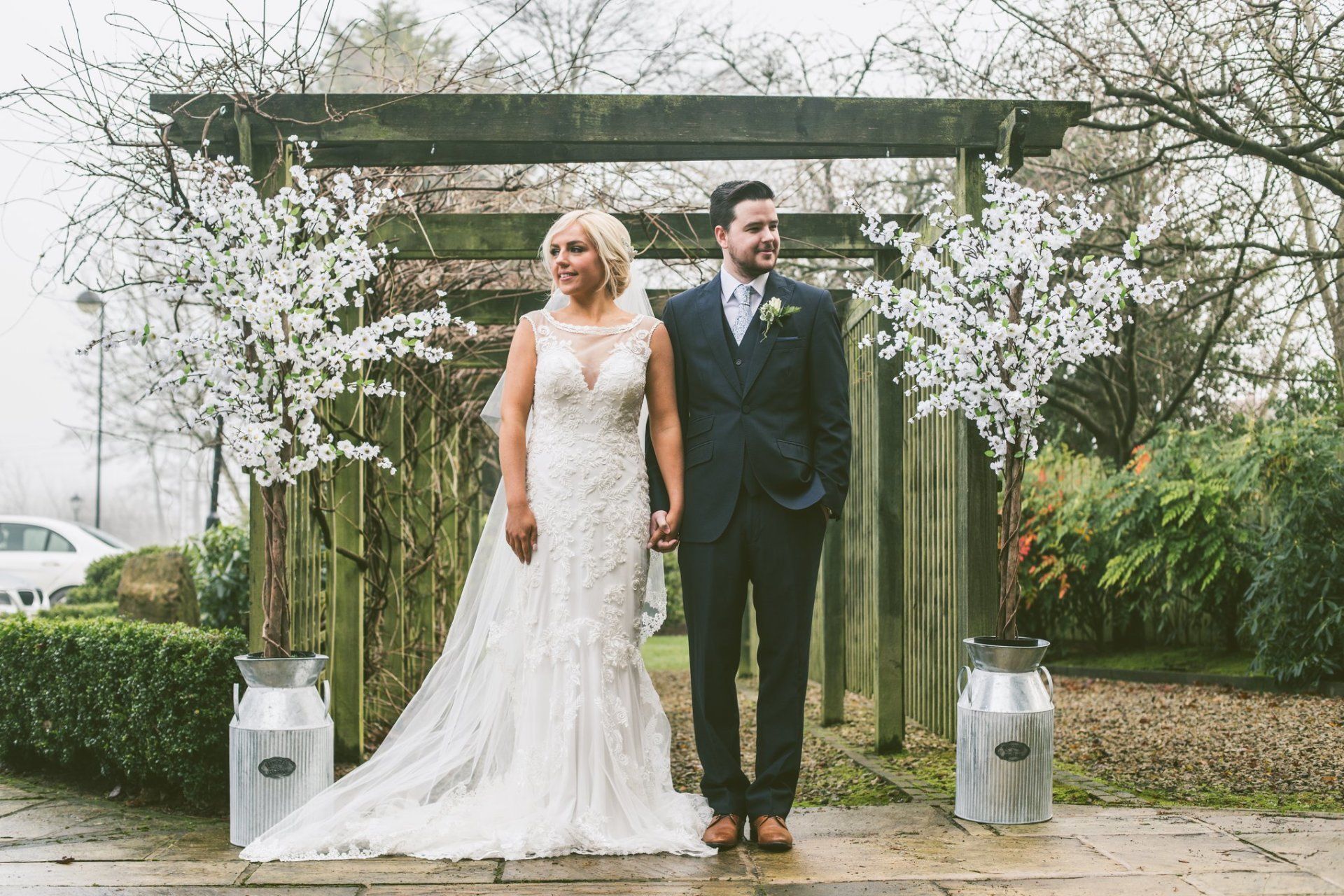 Bride and groom standing under a floral arch in an outdoor garden setting