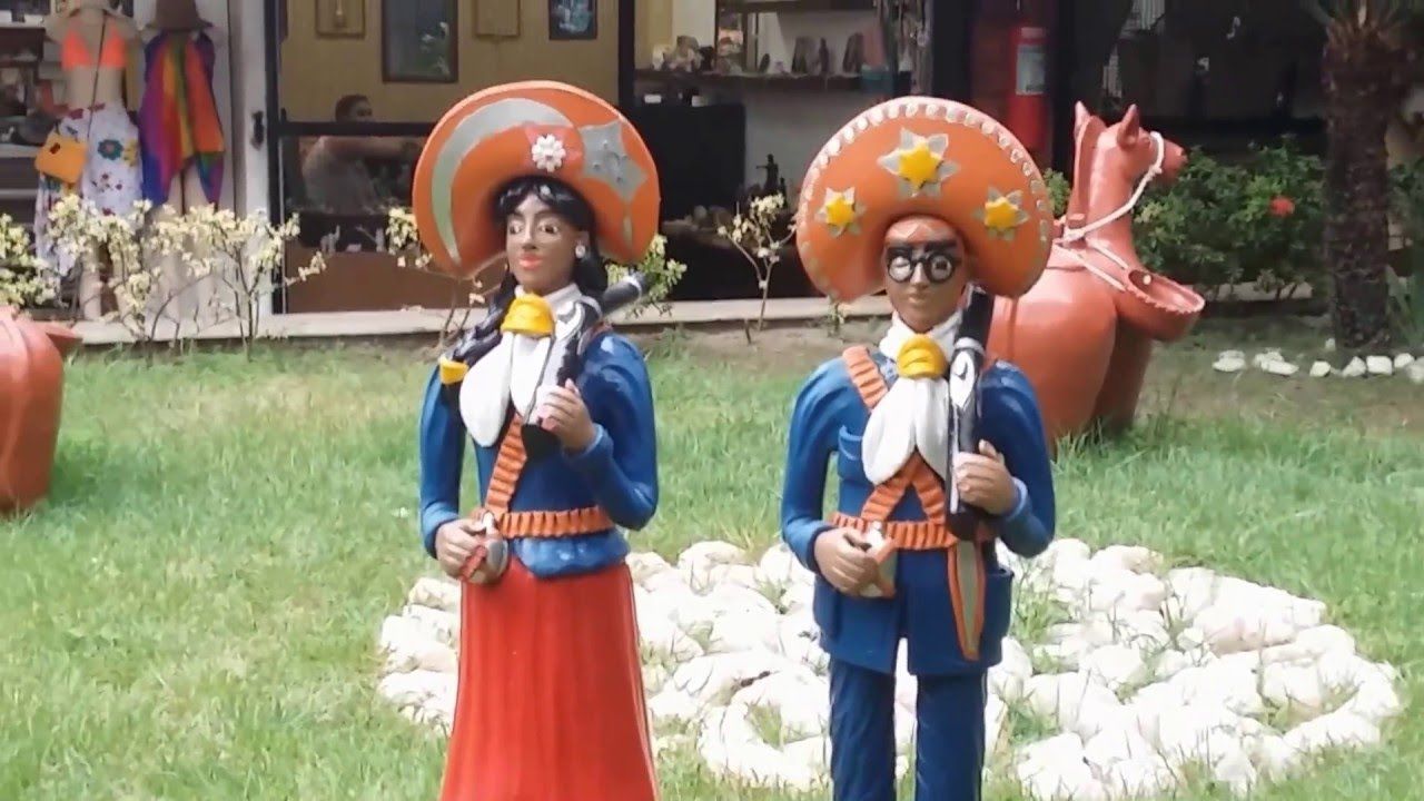 Duas estátuas decorativas vestindo cangaços coloridos, trajes tradicionais brasileiros, estão em um gramado em frente a uma loja.