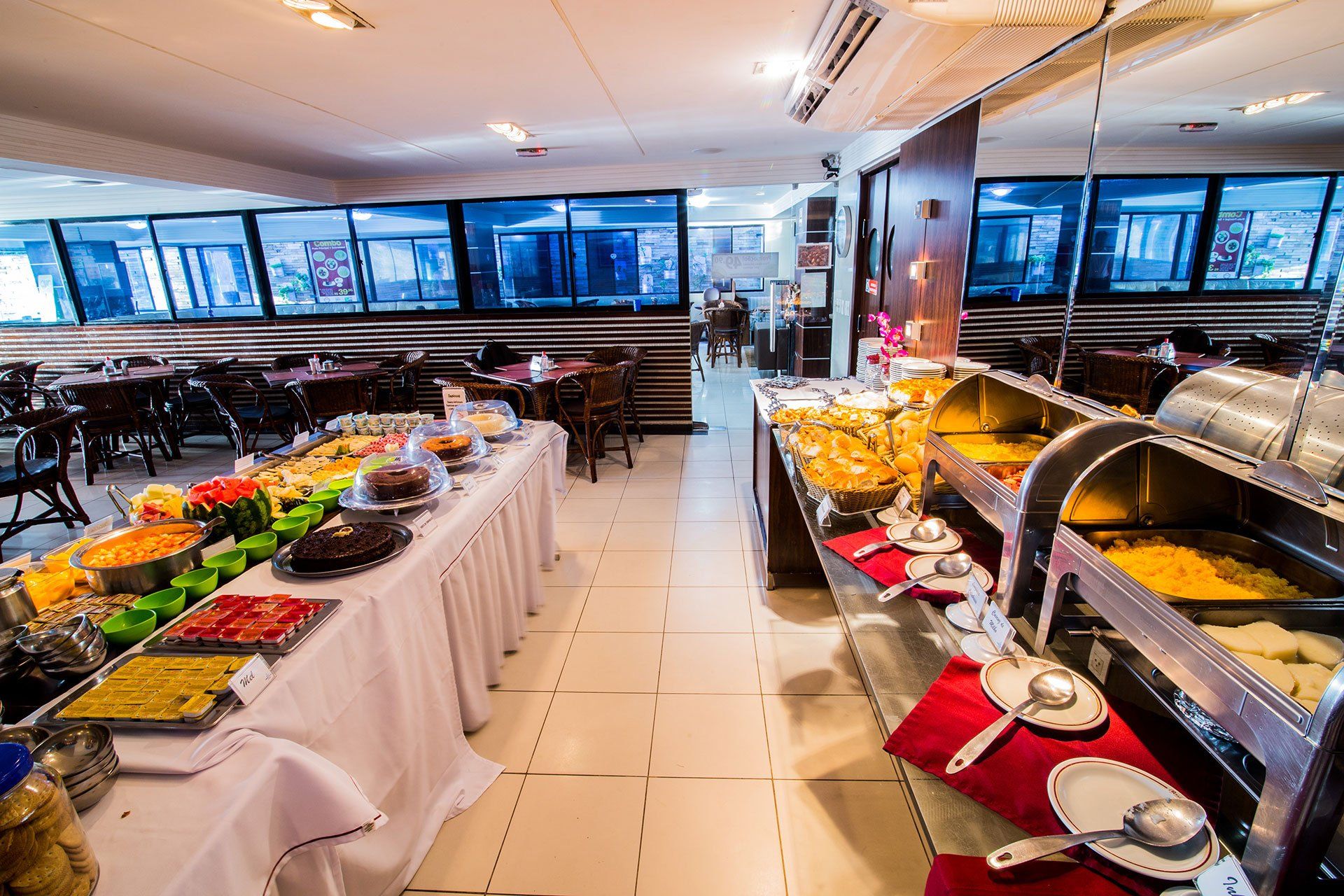 Uma área de buffet em um restaurante com mesas compridas repletas de diversos pratos prontos e estações de aquecimento.