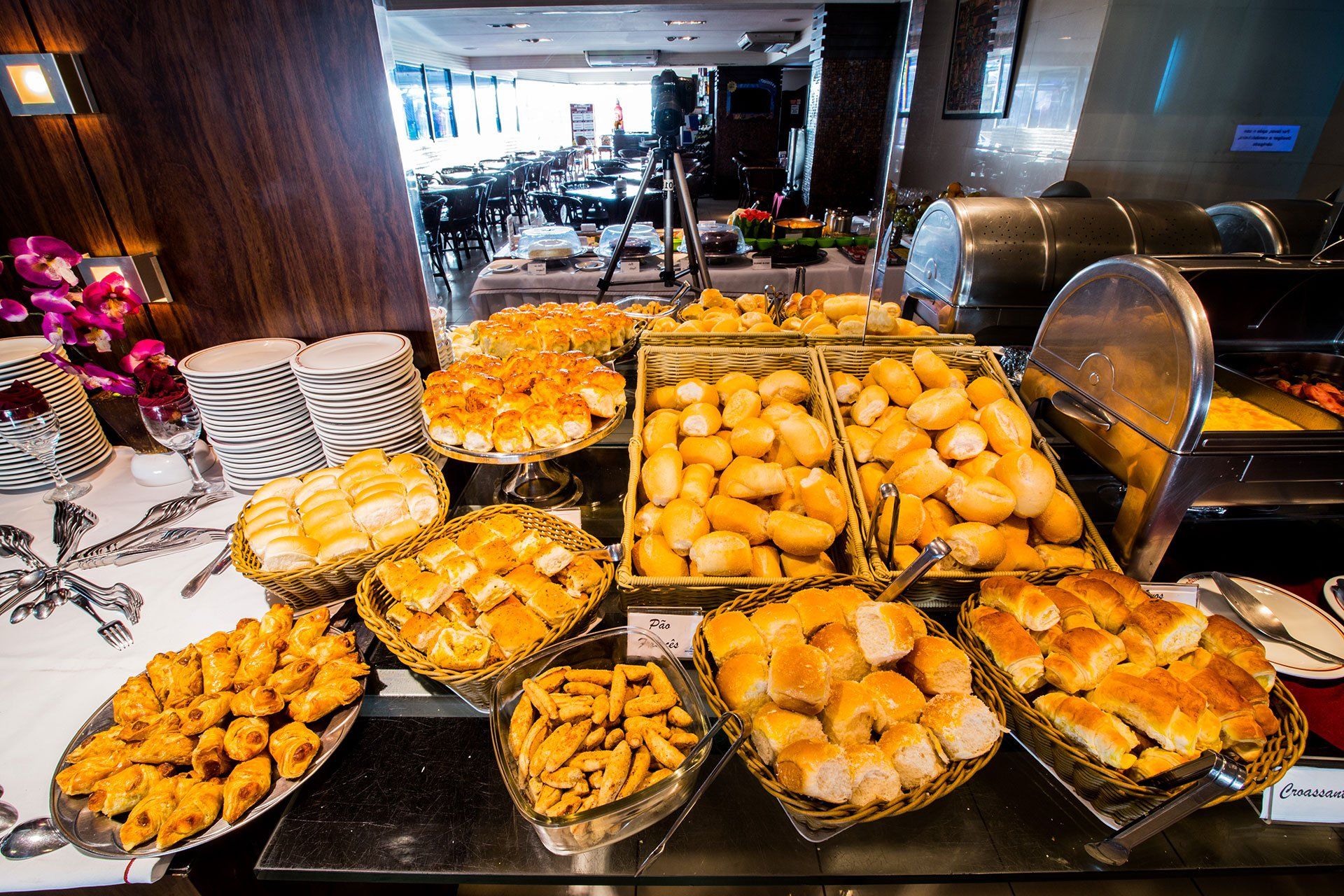 Uma variedade de pães e doces dispostos em cestas e bandejas em um buffet de café da manhã de hotel.