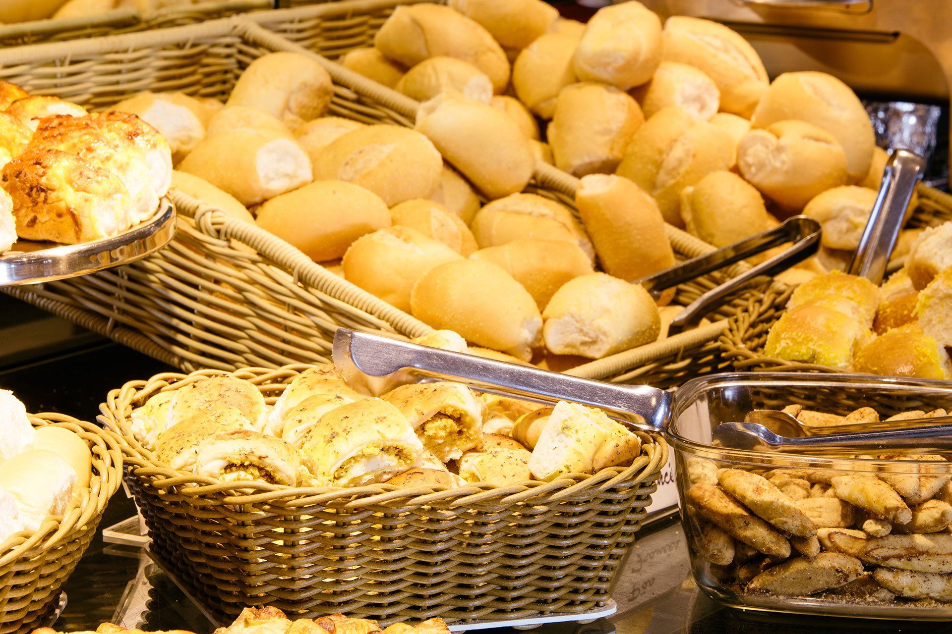 Cestas de vime repletas de pães e outros produtos de panificação em exposição numa padaria.