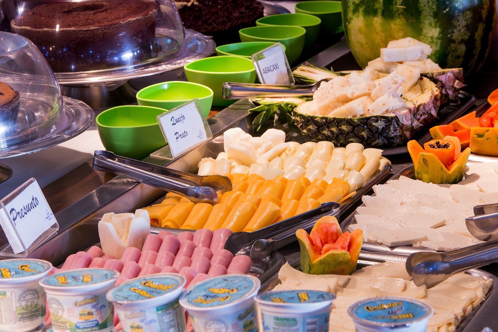 O buffet de café da manhã do hotel oferece uma variedade de queijos fatiados, frios, iogurtes, frutas e bolo de chocolate.