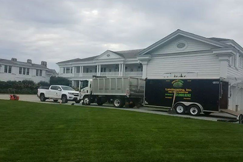 White pickup truck, dump truck, and trailer parked on grass in front of a white building.