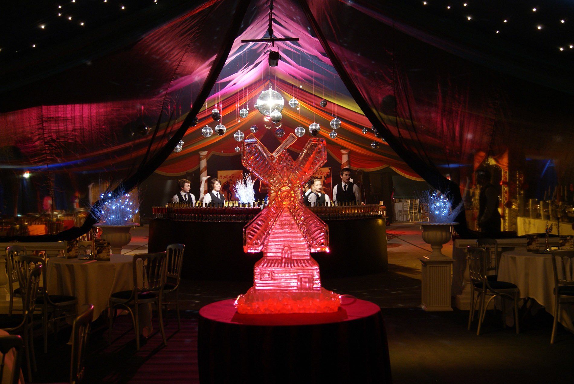 Red-lit banquet hall with draped ceiling and a glowing crystal sculpture centerpiece on a round table.