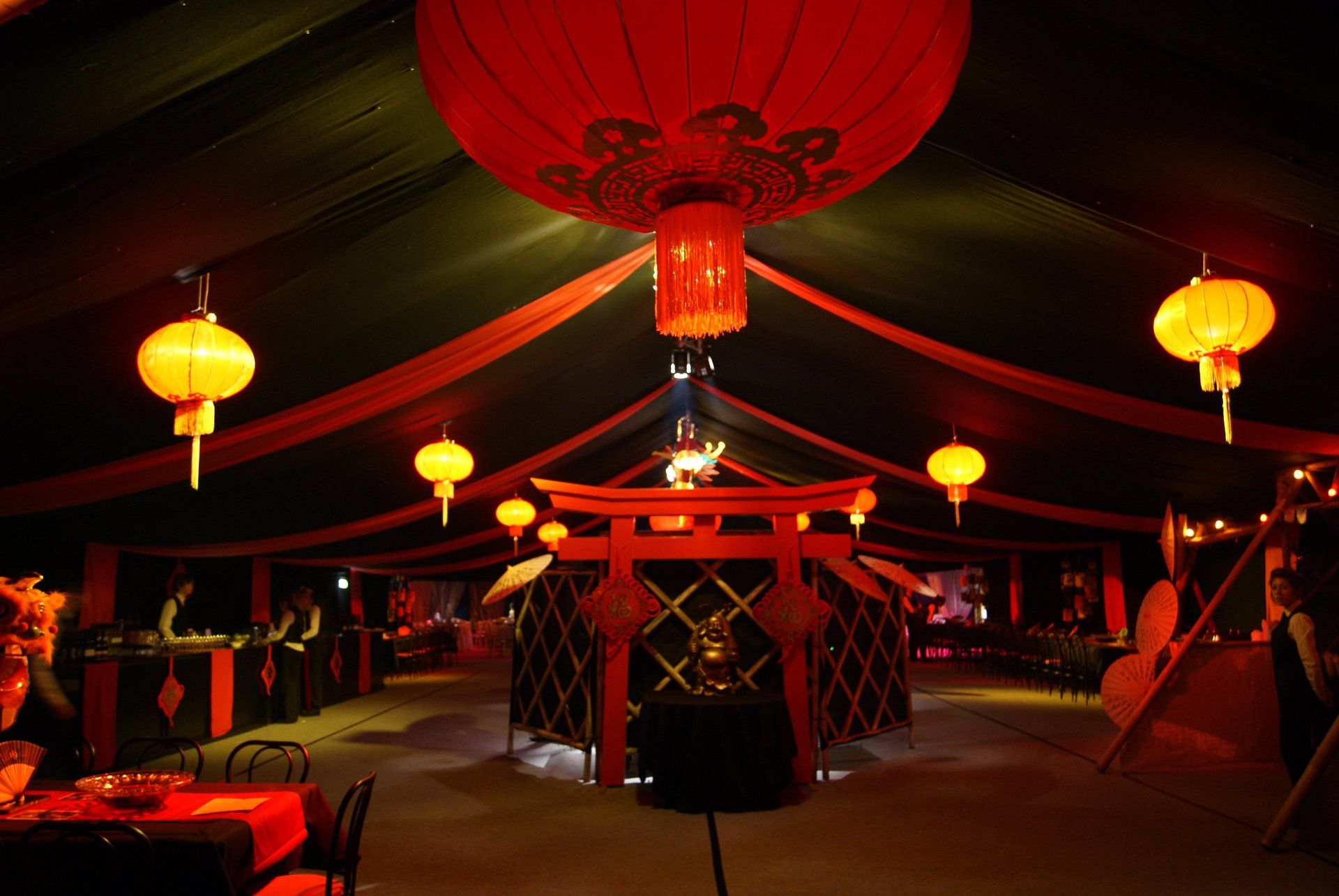 Red lantern-lit tent interior with a central stage and hanging decorations at night