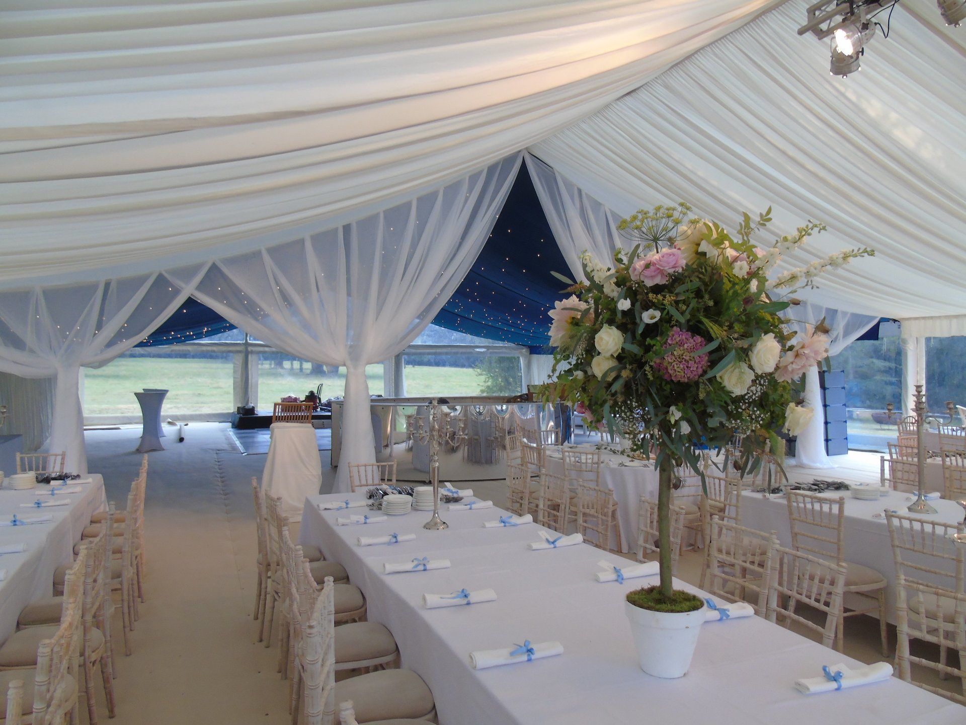 Elegant white-tented banquet setup with long tables, floral centerpieces, and ocean view at dusk