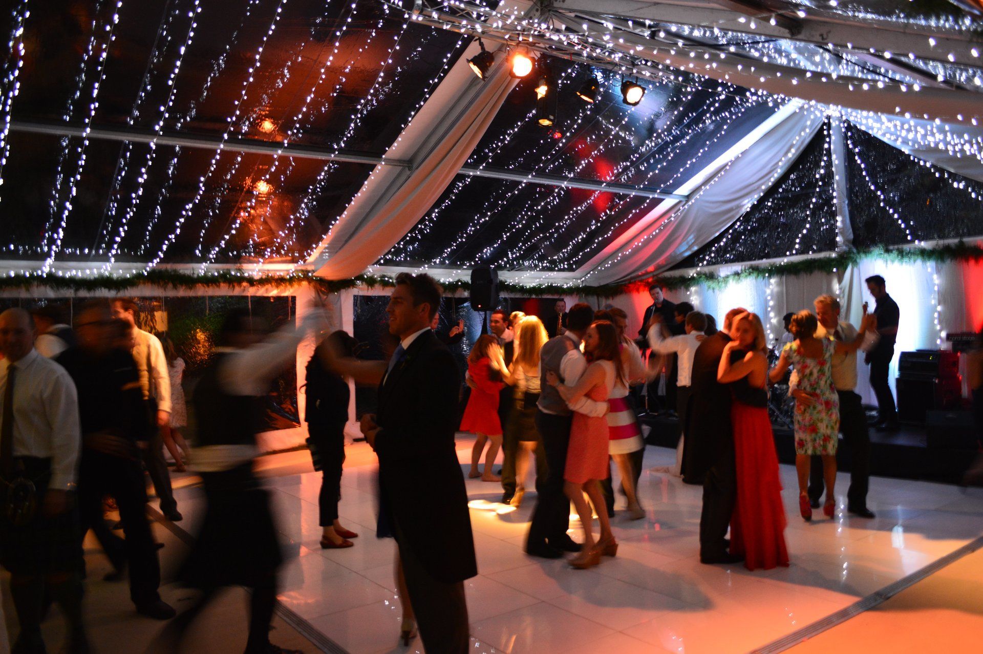 People dancing at a formal indoor event under string lights and draped white fabric.