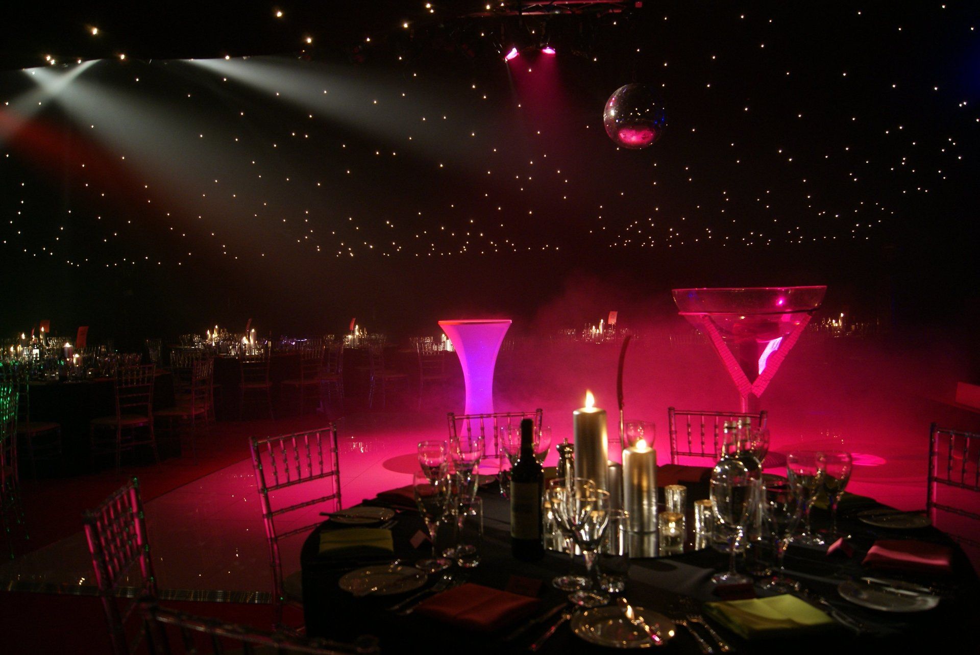 Pink-lit banquet table in a dark ballroom with starry ceiling lights and decorative centerpieces