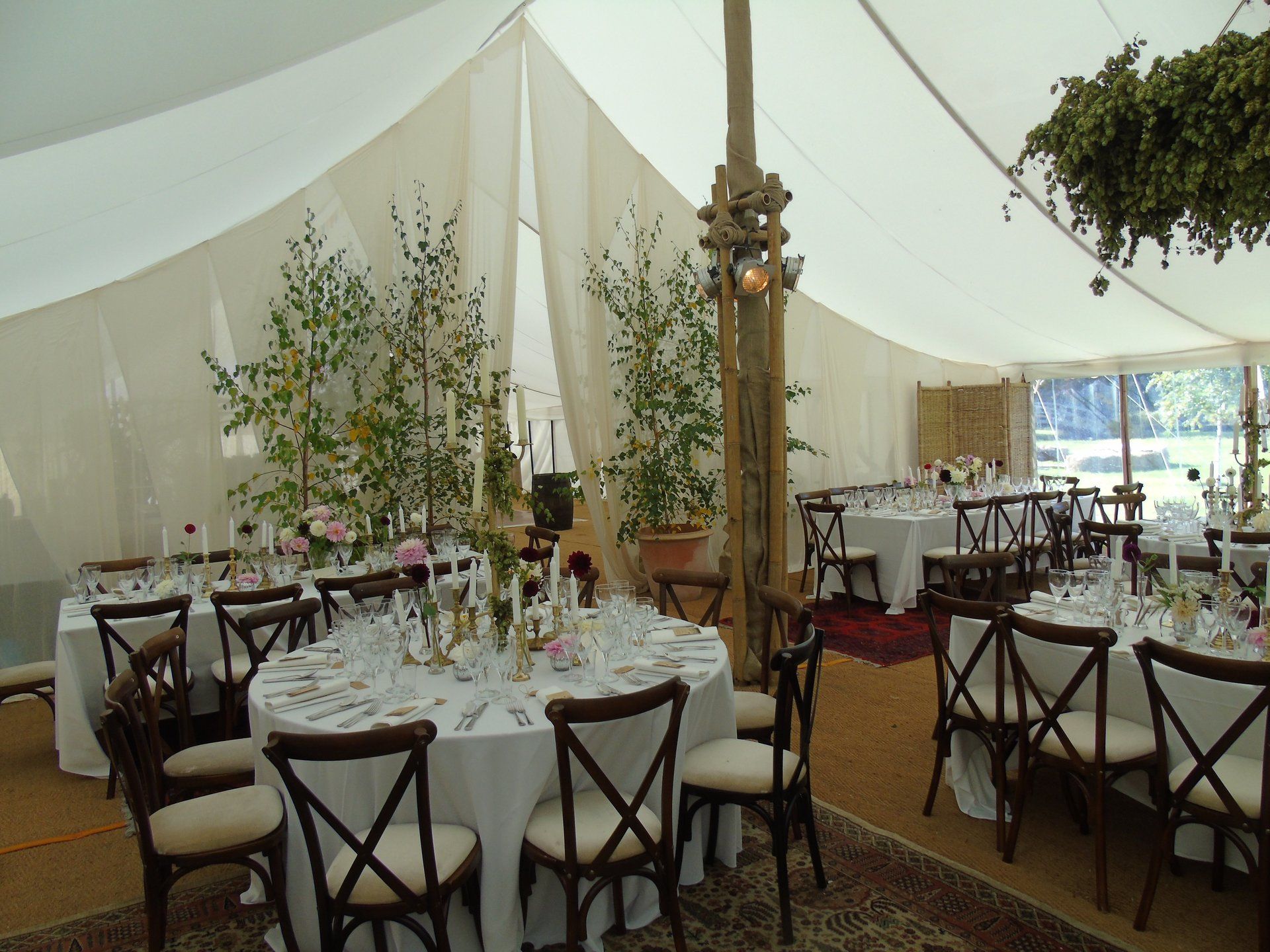 Elegant tented dining area with round tables, white linens, floral centerpieces, and dark wooden chairs