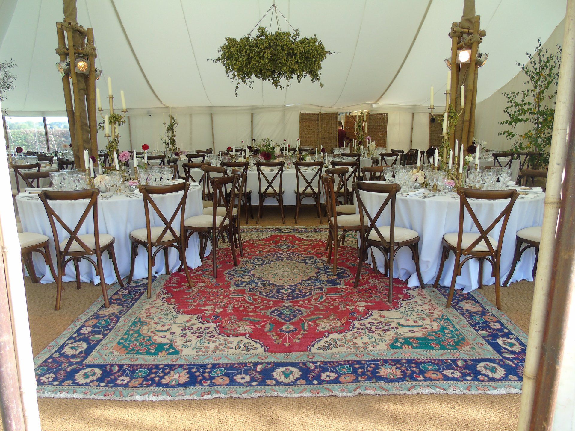 Elegant tented dining setup with round tables, white chairs, and red-blue patterned rugs