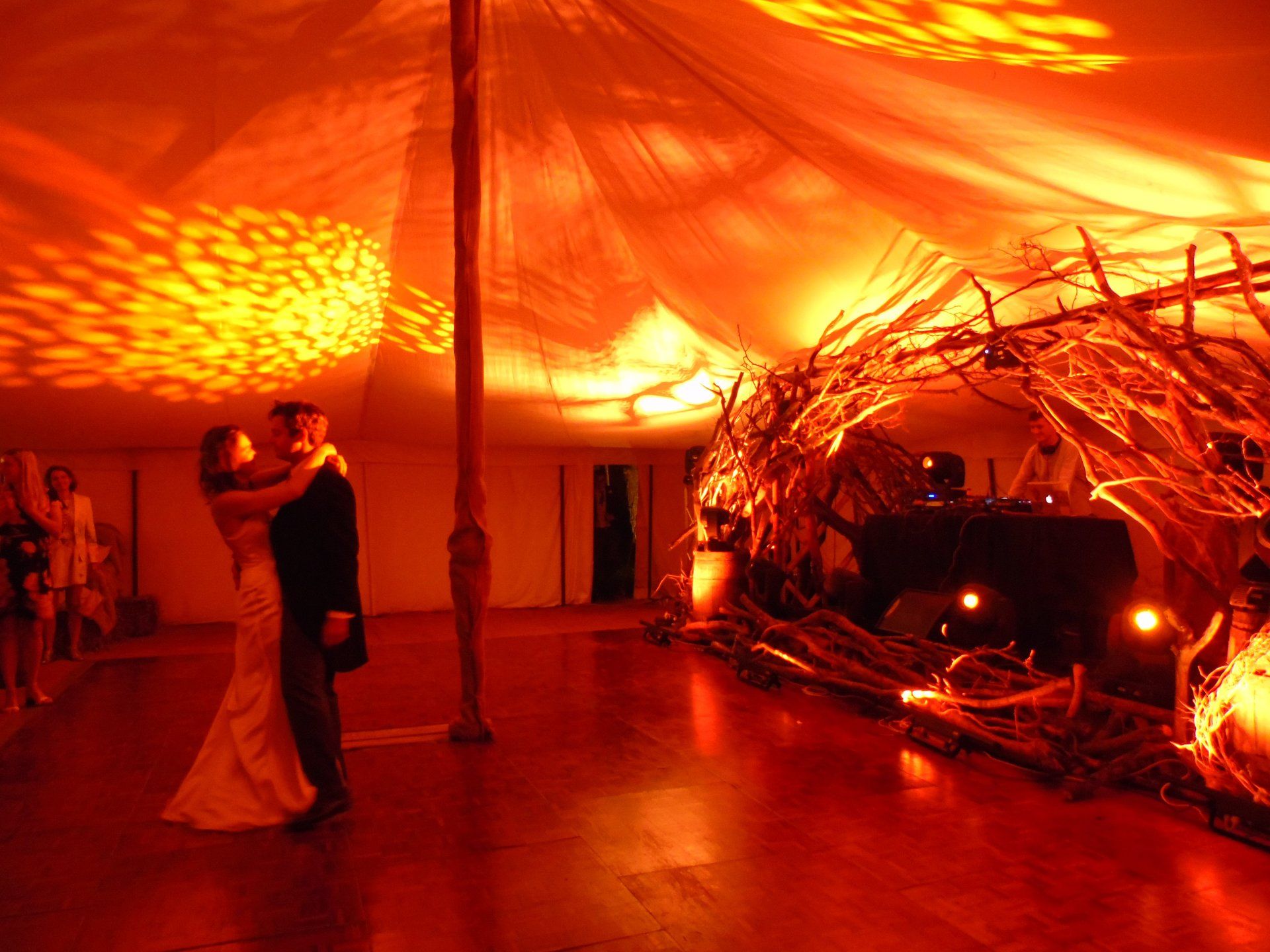 Couple dancing under orange patterned lights in a tented event space with woven decorations