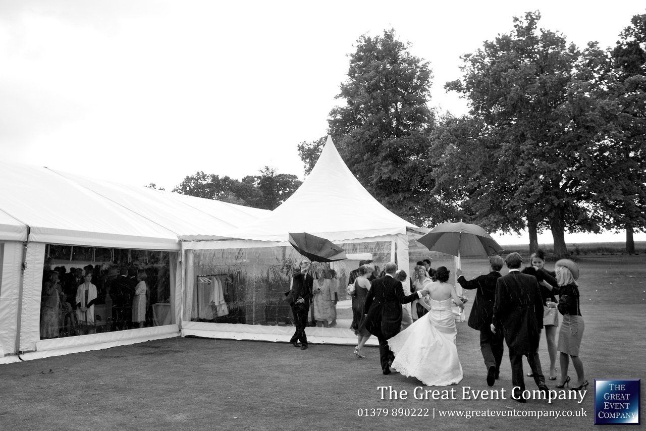 People walking near a white event tent and trees in an outdoor park setting