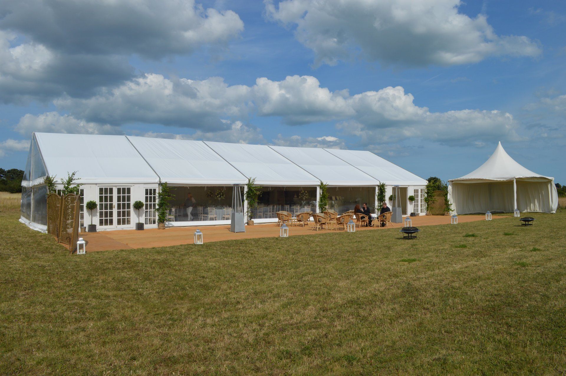 Large white event tent with open sides on a grassy field under a cloudy blue sky