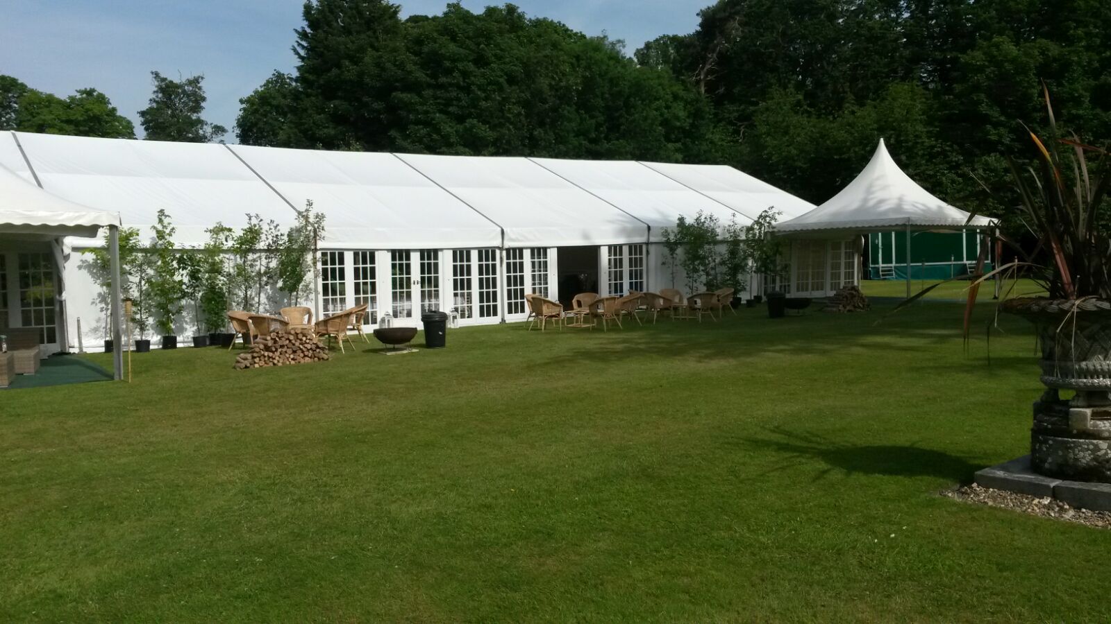 White event tent on a grassy lawn with tables and chairs beside a small canopy and trees