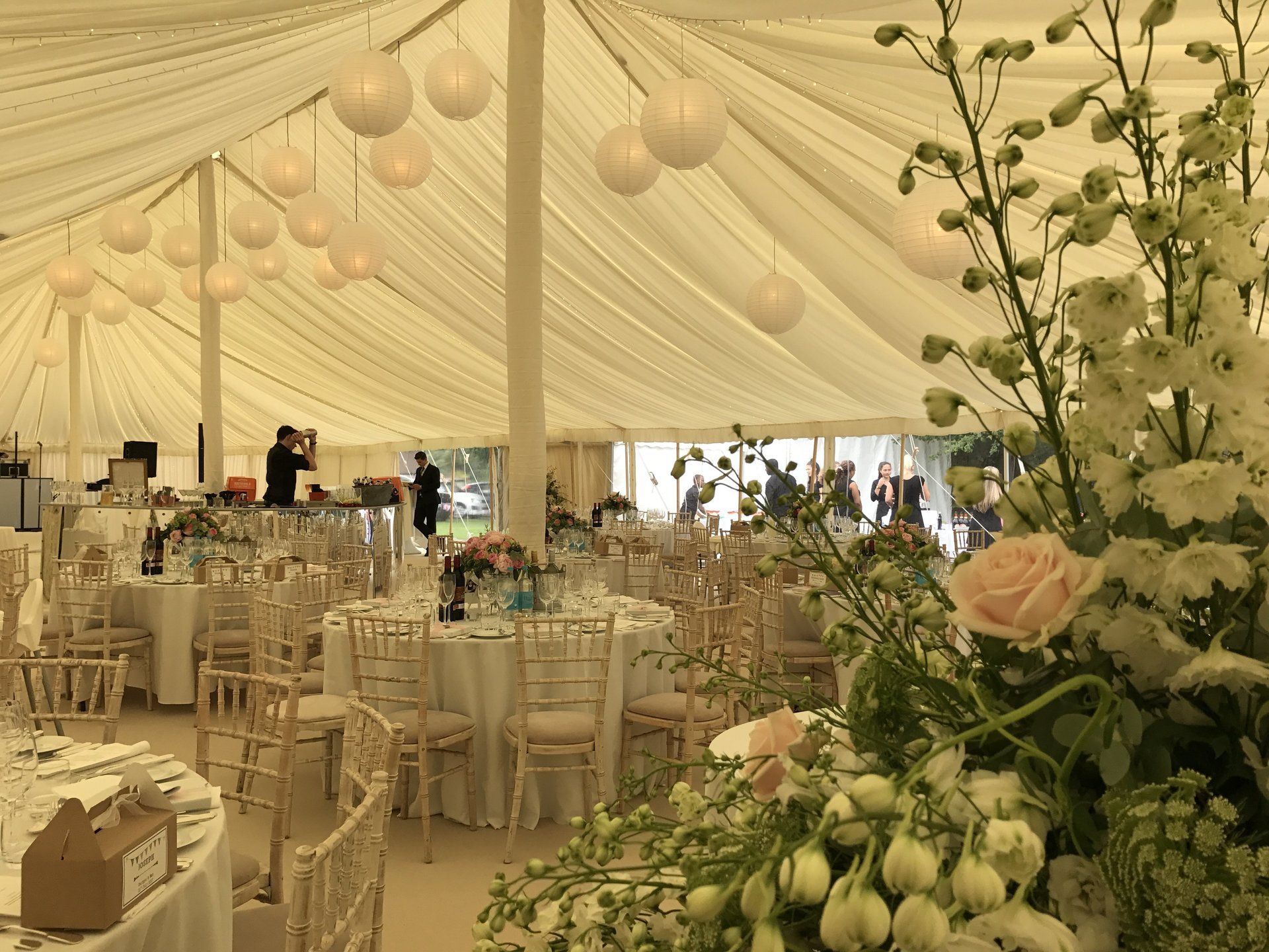 Elegant banquet tent with cream drapes, round tables, and white floral arrangements at a formal event