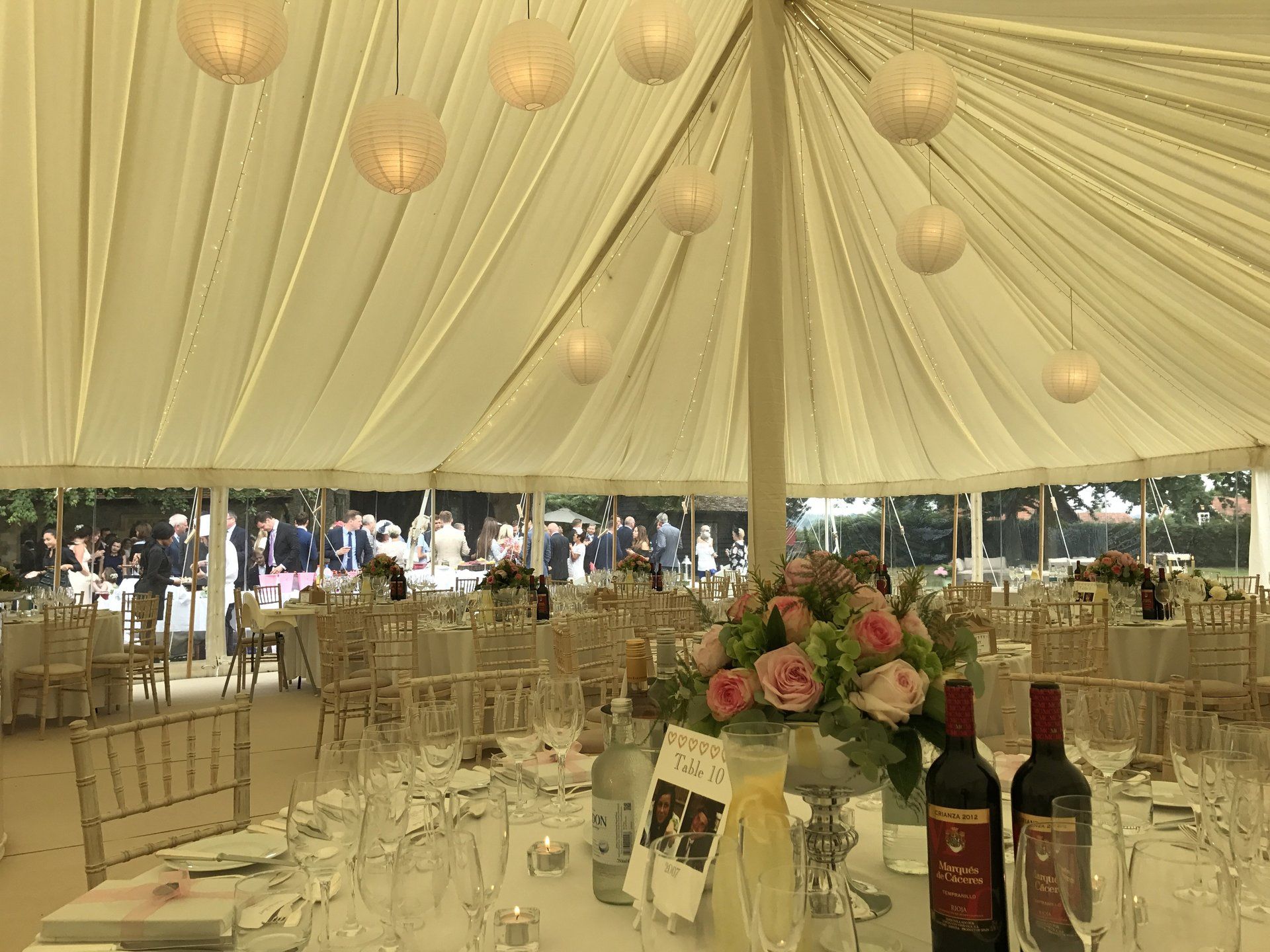 Elegant banquet tent with draped cream ceiling, round tables, floral centerpieces, and wine bottles set for an event