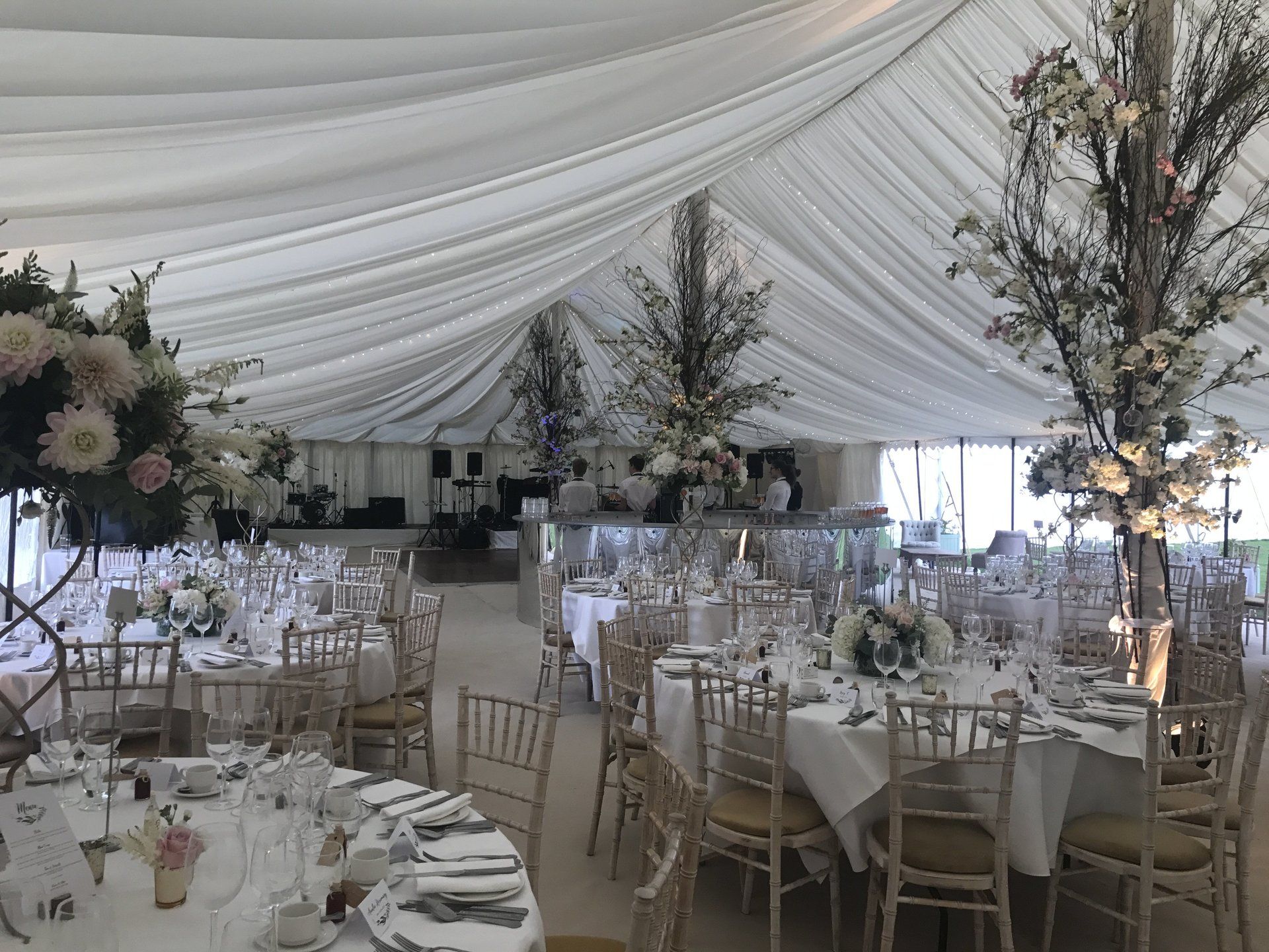 Elegant banquet hall with white draped ceiling, round tables, glassware, and floral centerpieces