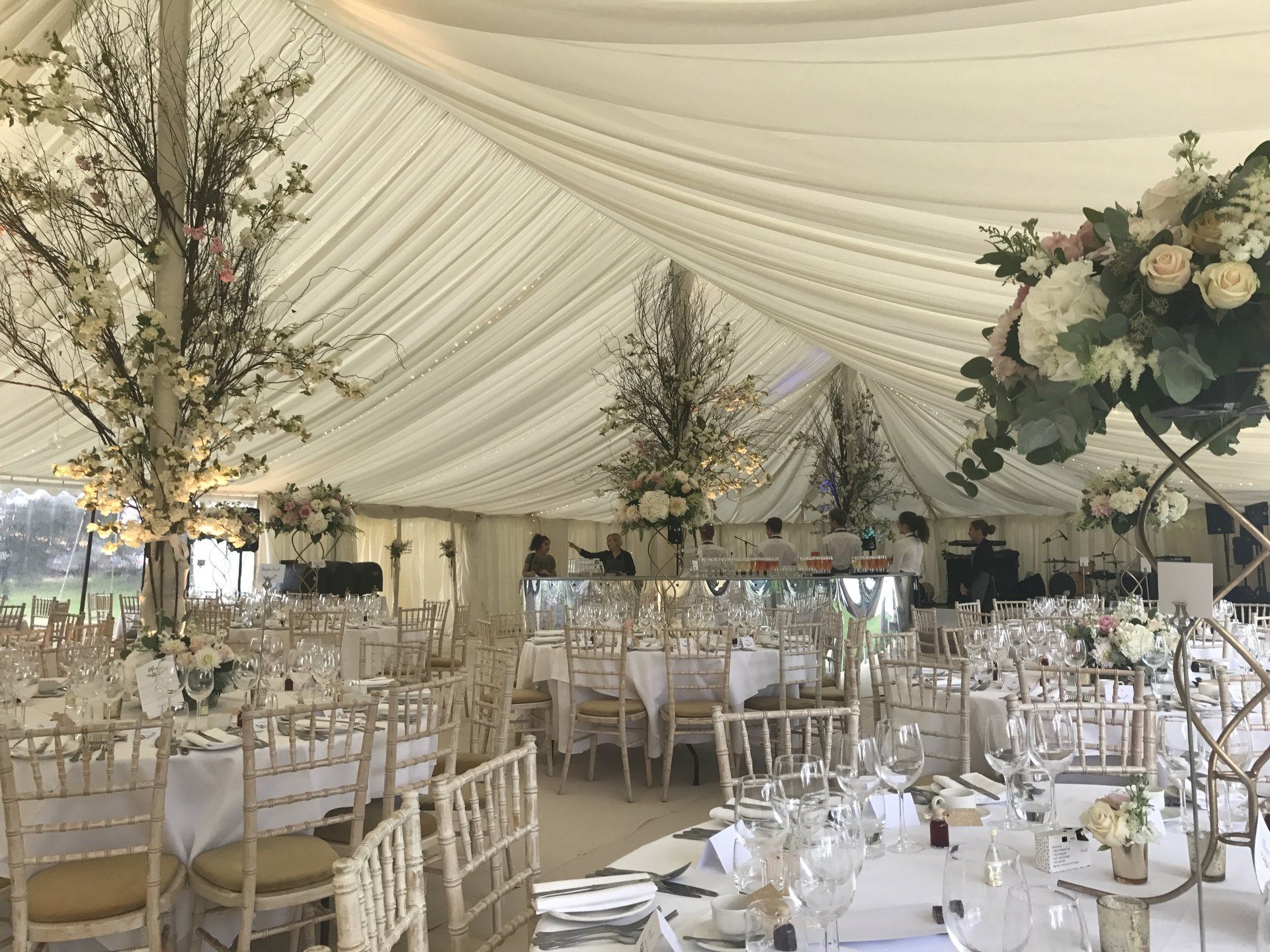Elegant wedding reception under a draped cream tent with white tables, chairs, and floral centerpieces