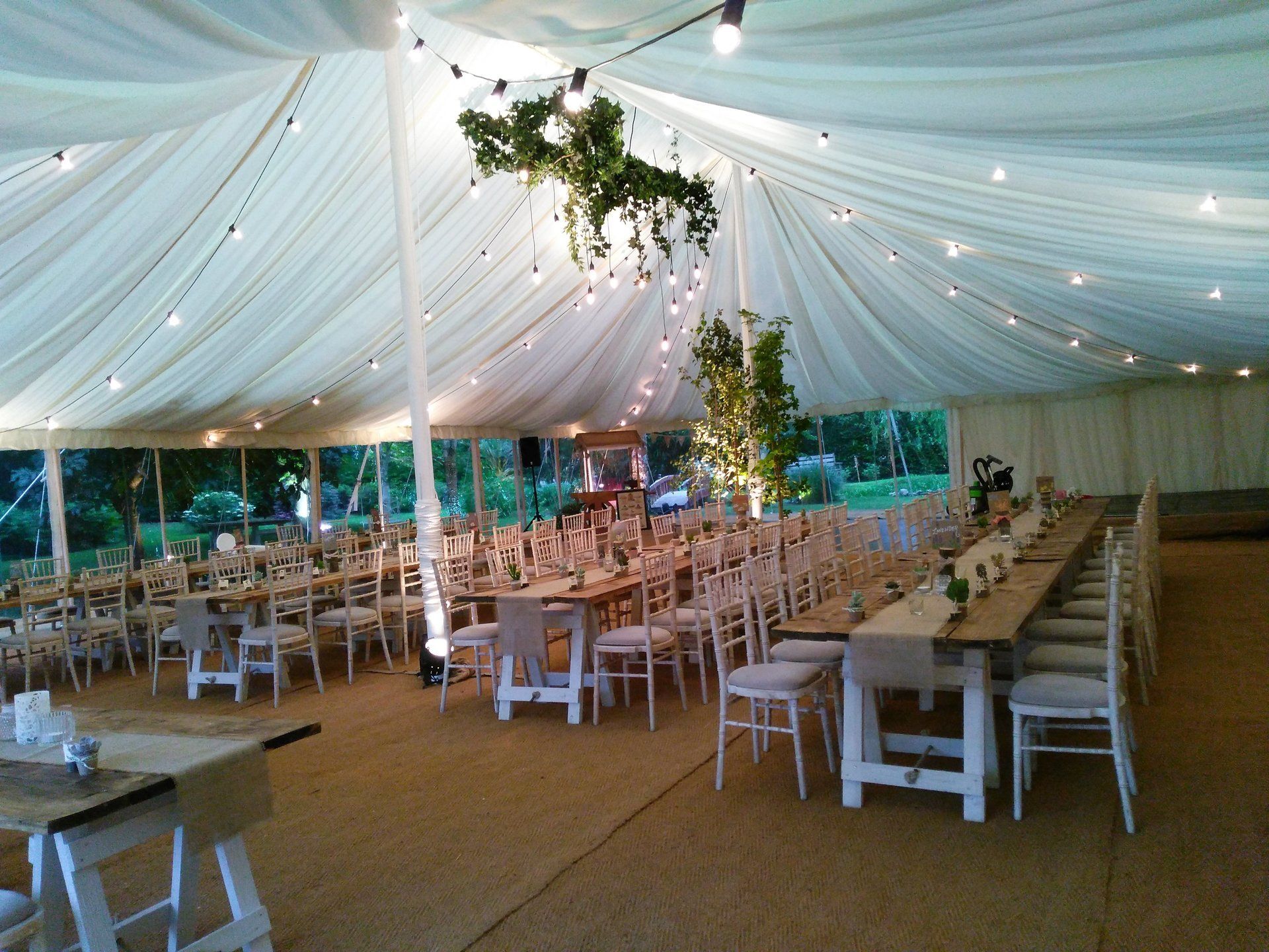 White-draped wedding tent with string lights, long tables, and chairs set for a reception