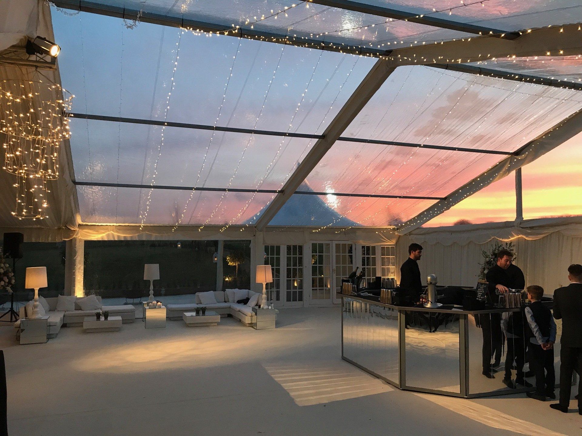 Rooftop lounge at sunset with string lights, modern seating, and people gathered at a bar area.