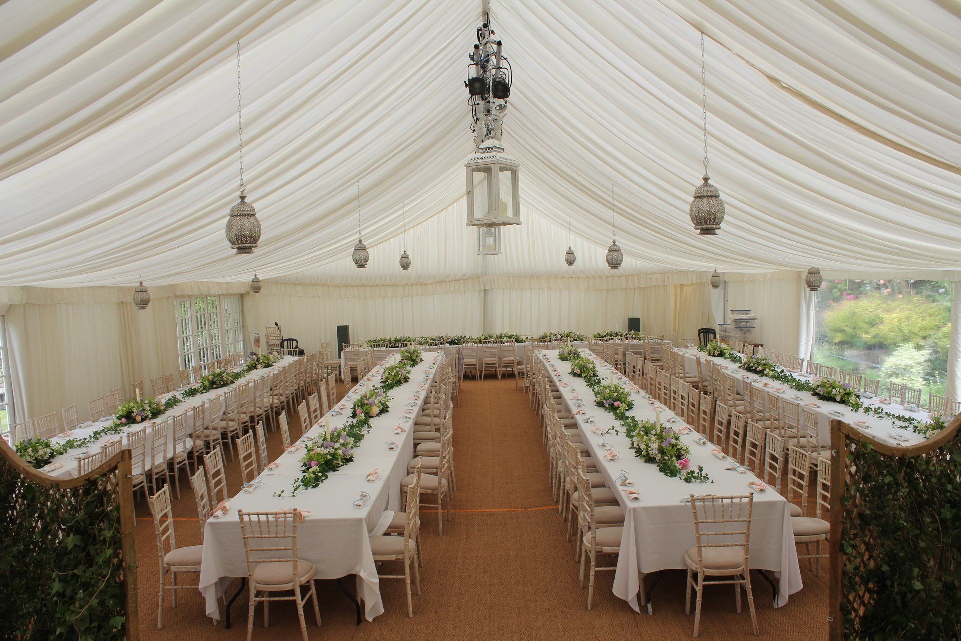 Elegant white wedding reception tent with long banquet tables, chandeliers, and green floral centerpieces
