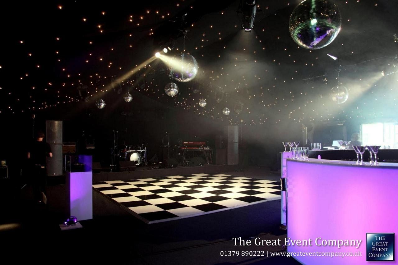 Dim nightclub with checkerboard floor, disco lights, and mirror balls under a dark ceiling.