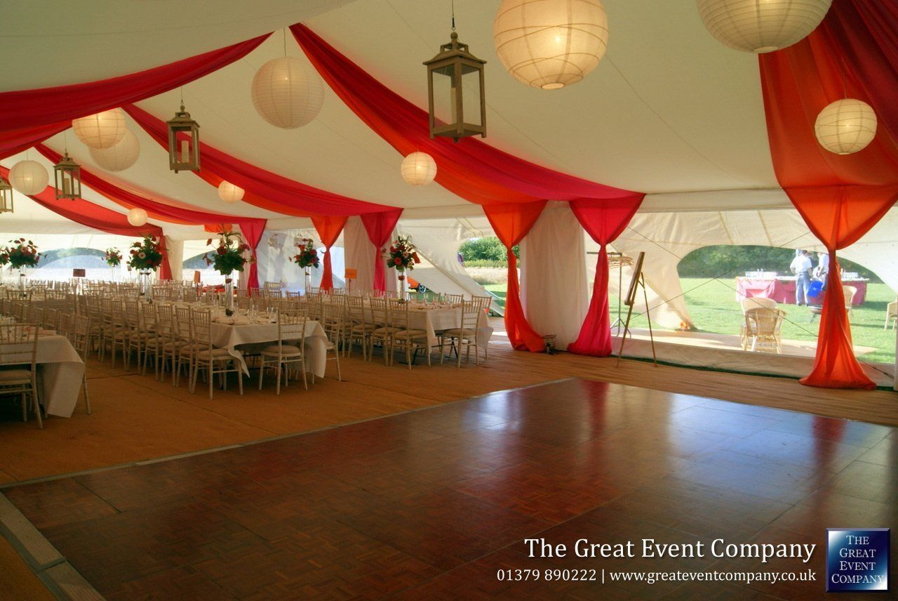 Red-and-white decorated wedding tent with banquet tables, hanging lanterns, and a dance floor